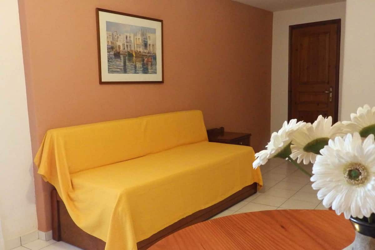 A room with a yellow sofa, a wooden table, and a vase with white flowers.
