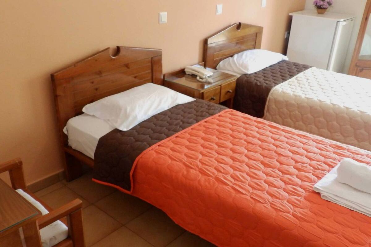 A room with two beds, a wooden headboard, a nightstand with a phone, a small table, and a chair.
