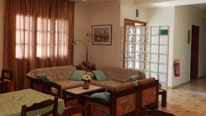 A living room with a sofa, chairs, a dining table, and a decorative vase. - Alexandra Hotel (Chania)
