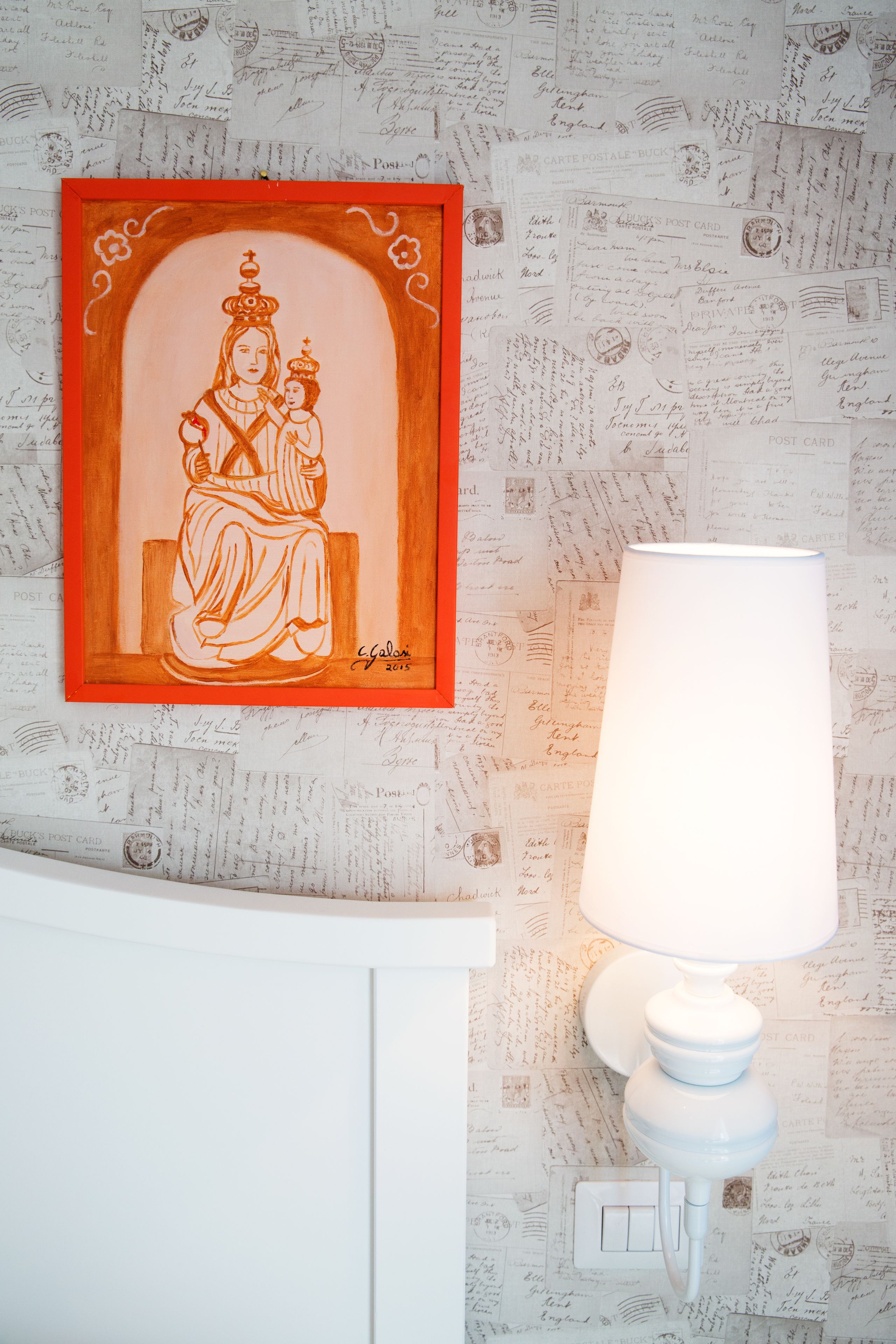 Ein gerahmtes Bild einer sitzenden Person an einer Wand, neben ihr eine weiße Lampe.
