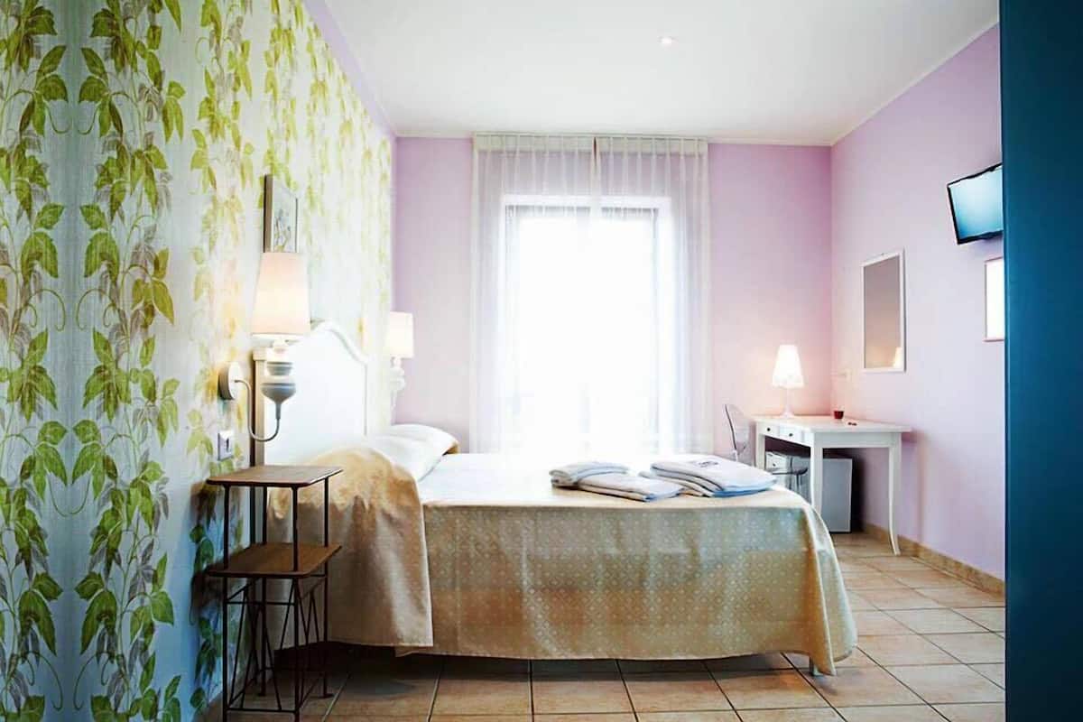 Une chambre d’hôtel avec un lit, un bureau, une chaise et un téléviseur fixé au mur.