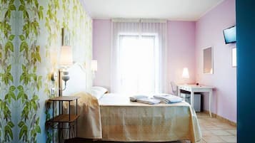 Une chambre d’hôtel avec un lit, un bureau, une chaise et un téléviseur fixé au mur.