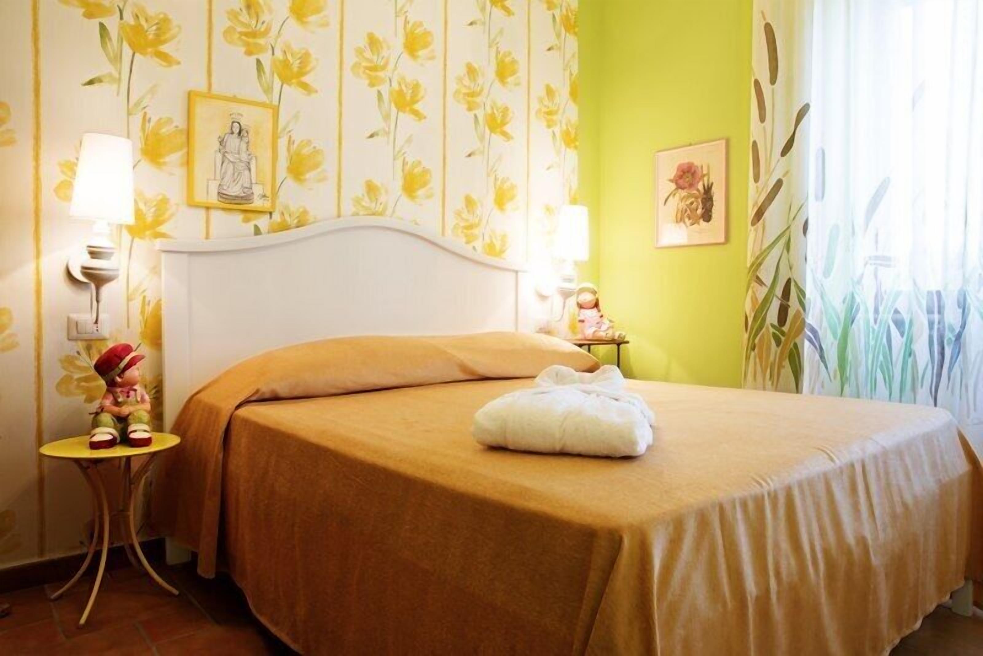 Een hotelkamer met een bed, een nachtkastje, een lamp en een wand met bloemenbehang.