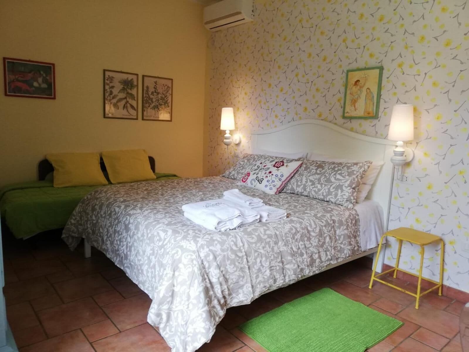 A bedroom with a bed, two bedside tables, a green rug, and patterned wallpaper.