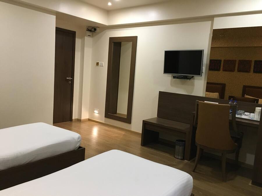Habitación de hotel con dos camas, un escritorio, una silla, un televisor y un espejo montado en la pared.