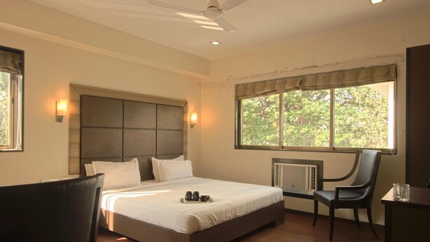A bedroom with a large bed, a chair, a desk, and a window with a view of trees.