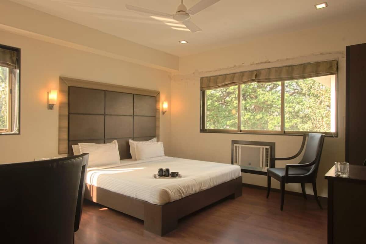 A bedroom with a large bed, a chair, a desk, and a window with a view of trees.