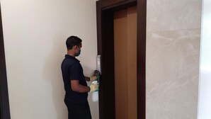 A person standing in a hallway, holding a spray bottle and a cloth, near a door with a marble finish.