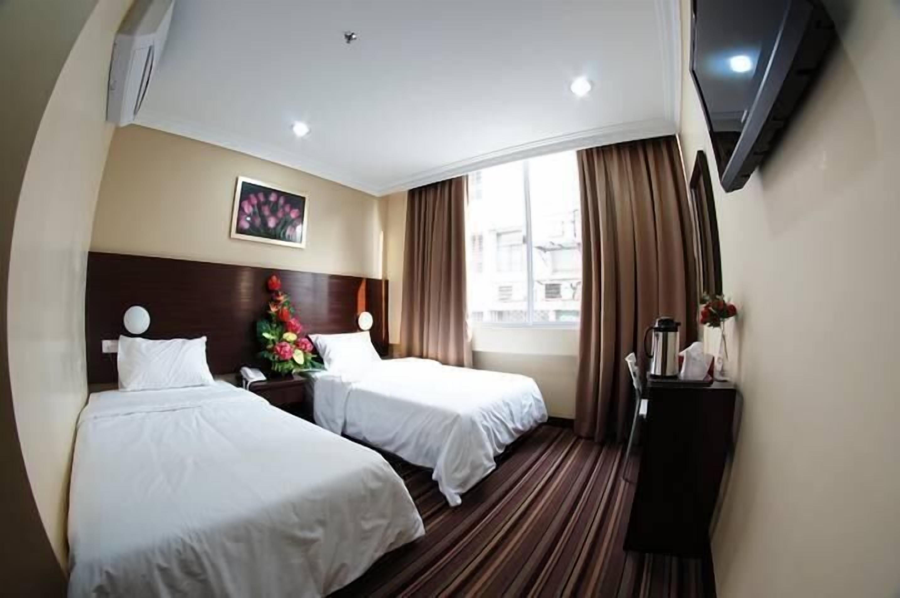 A hotel room with two beds, a large window with curtains, a painting on the wall, and a TV mounted on the wall.