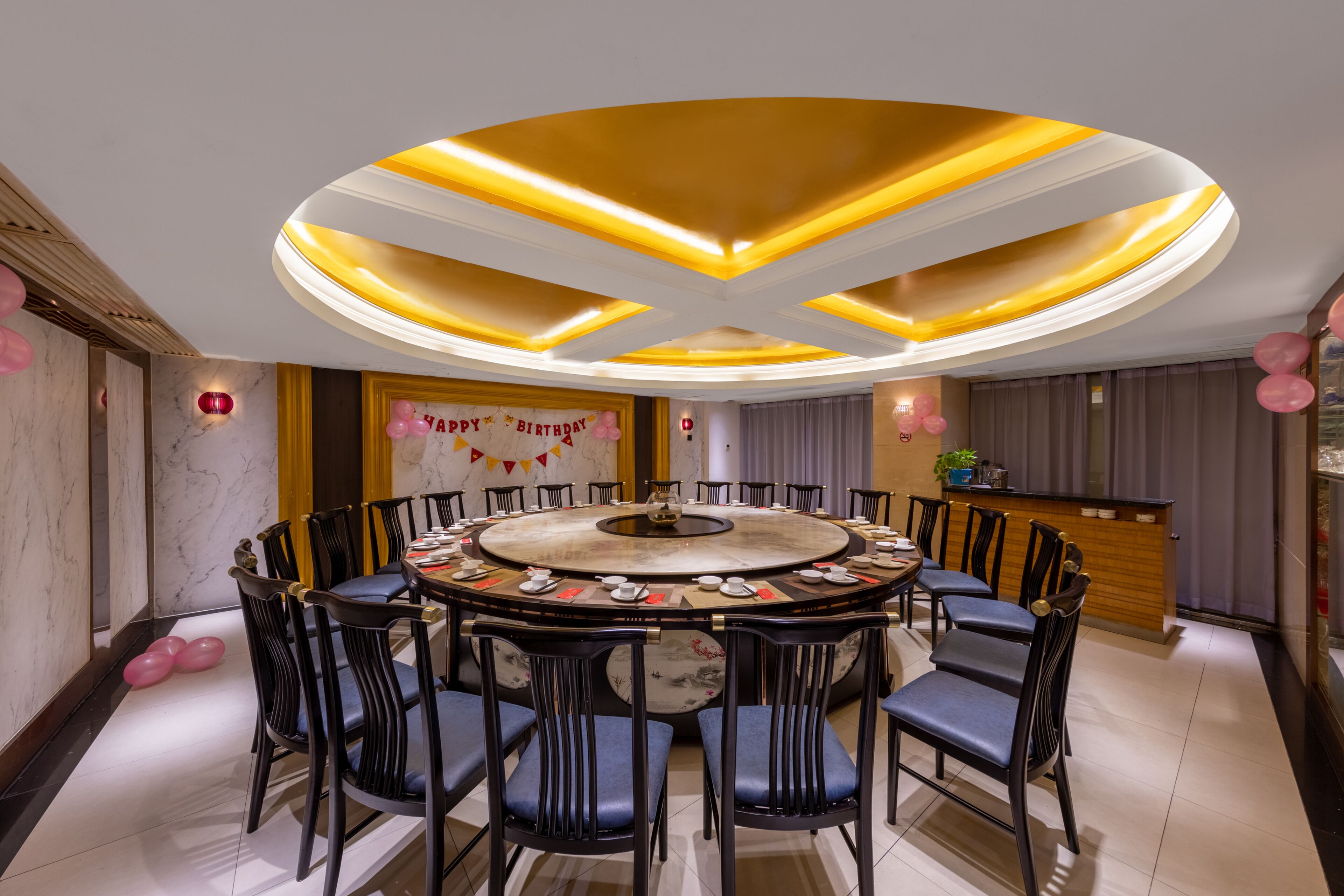 A round dining table with chairs, a central decorative piece, and a banner with "Happy Birthday" text.