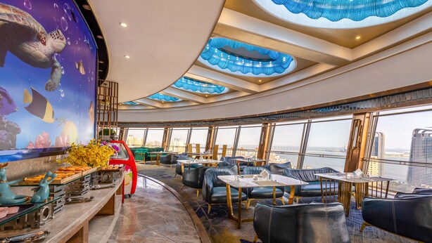 A restaurant with a view of the city skyline, featuring a ceiling with blue decorative elements and a mural of sea creatures. - Guangdong Hotel Zhuhai (Zhuhai)
