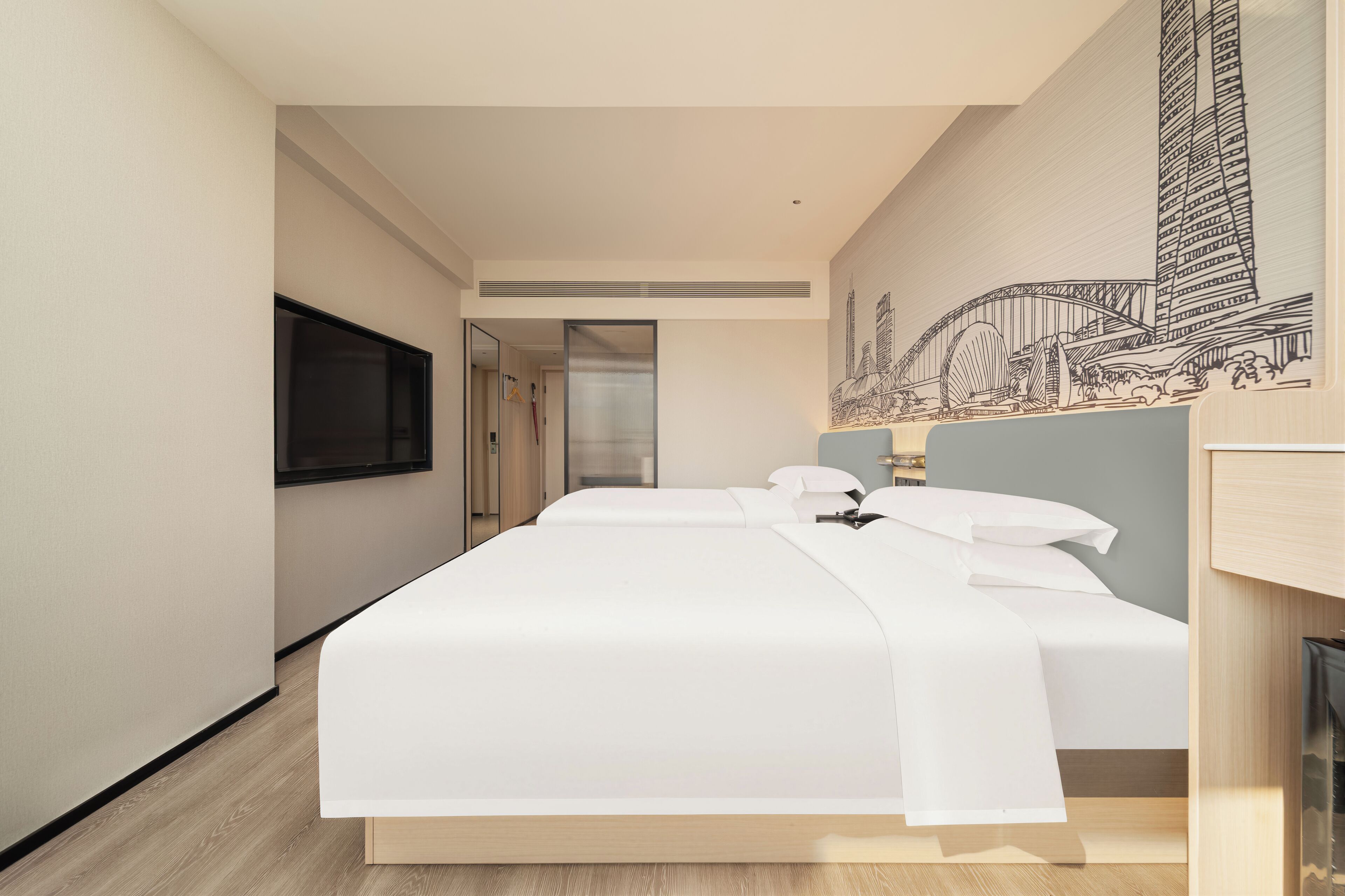 Camera d'albergo moderna con un ampio letto, una TV a schermo piatto e un murale raffigurante un panorama urbano.