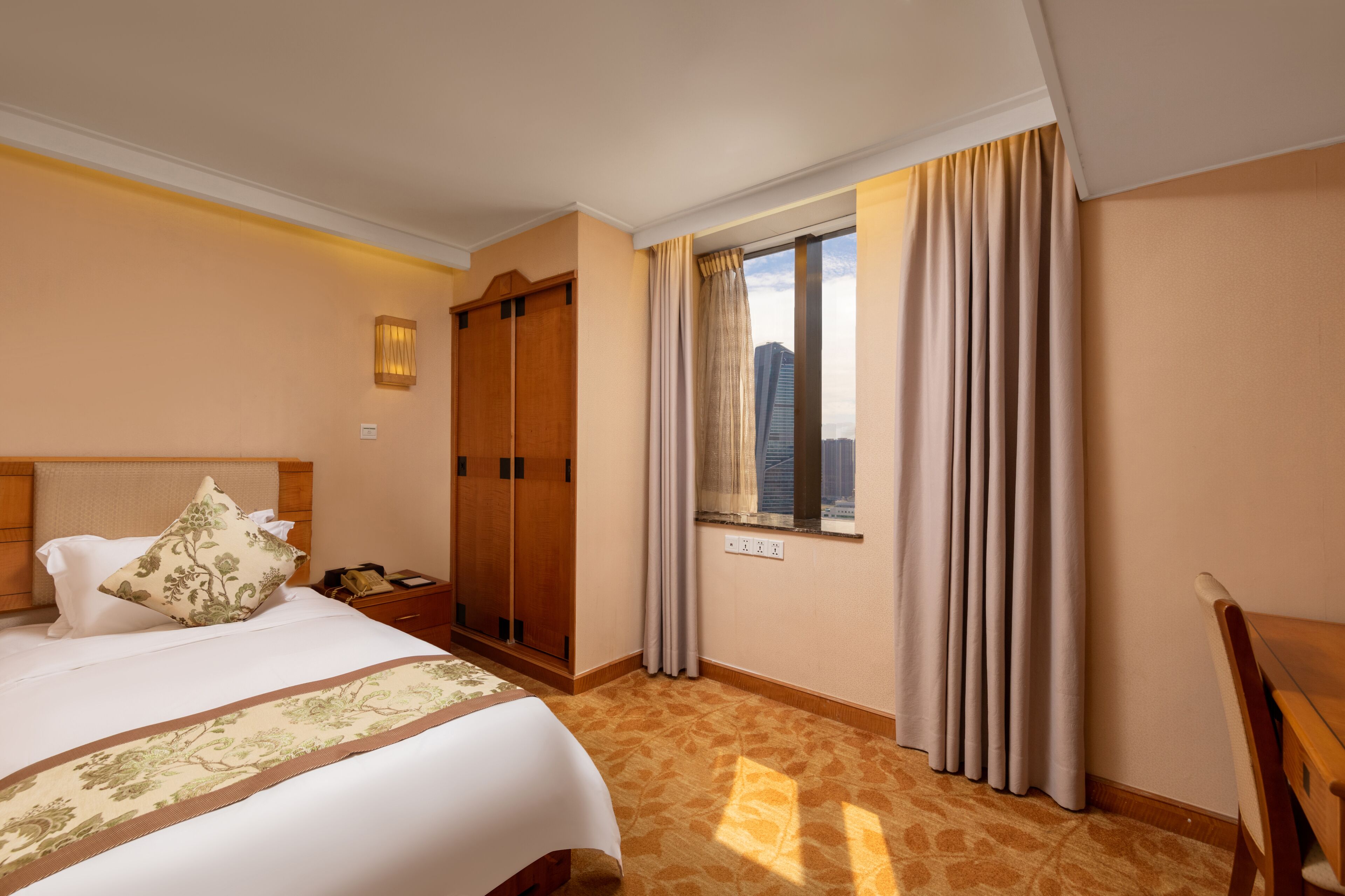 A hotel room with a bed, a wardrobe, a nightstand, and a window with curtains.