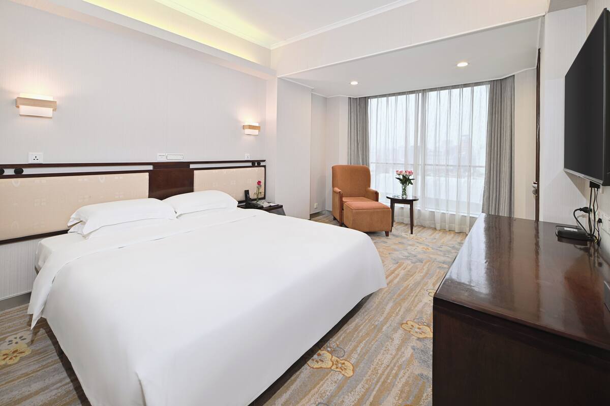 Ein Hotelzimmer mit einem großen Bett, einem Schreibtisch, einem Stuhl und einem Fernseher.