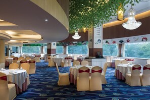 Un salón de banquetes con mesas redondas, sillas adornadas con cintas rojas y plantas colgantes.