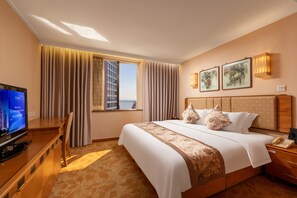 Habitación de hotel con una cama grande, un escritorio con ordenador, televisor y vista a un edificio.
