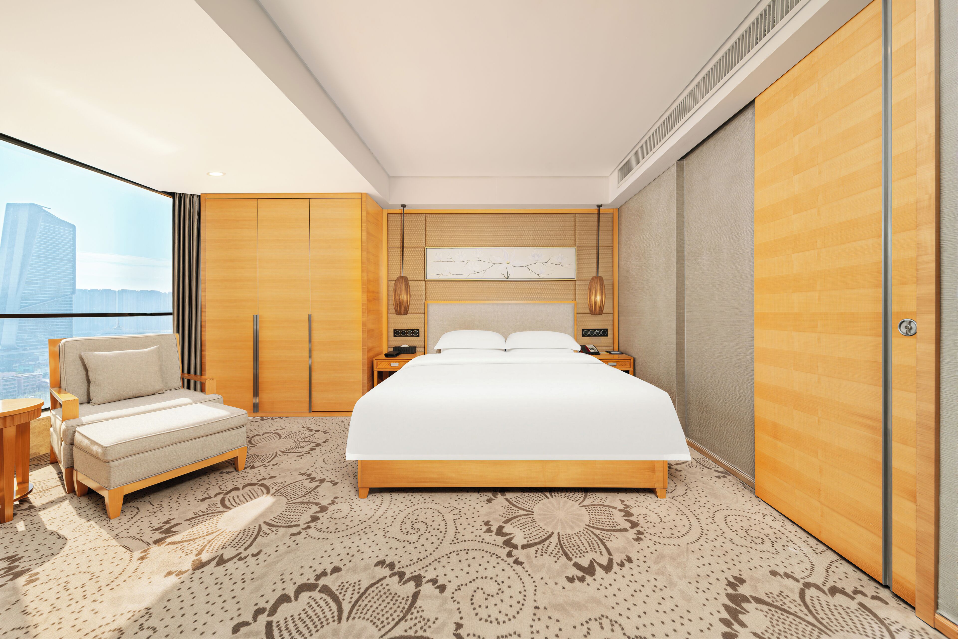 A modern hotel room with a large bed, a sofa, a desk, and a view of the city.