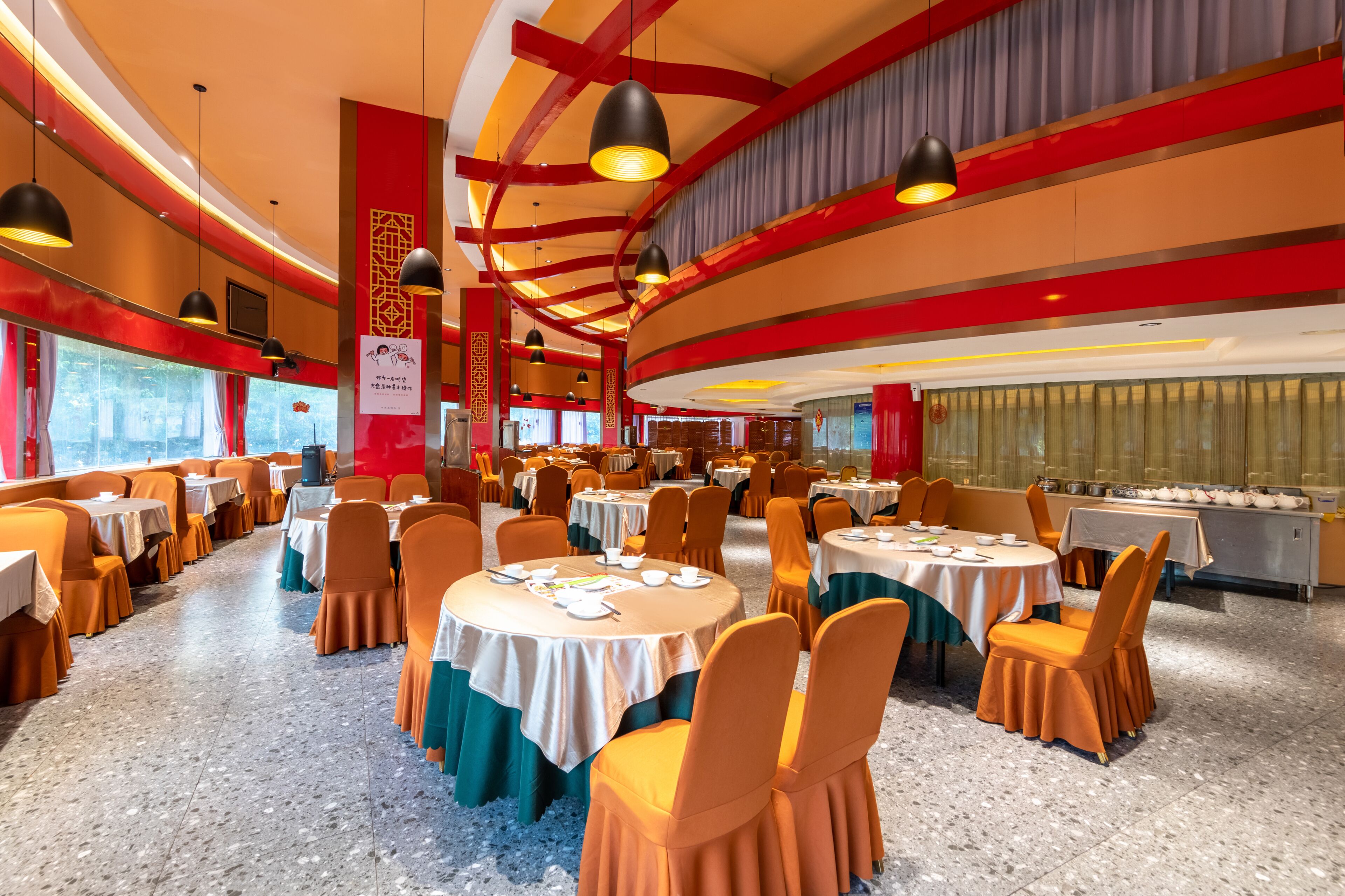 A banquet hall with round tables, orange chairs, and a red and gold color scheme.