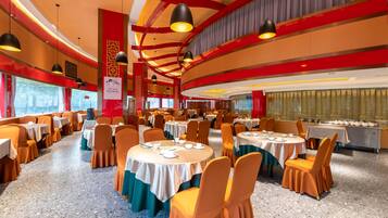 A banquet hall with round tables, orange chairs, and a red and gold color scheme.