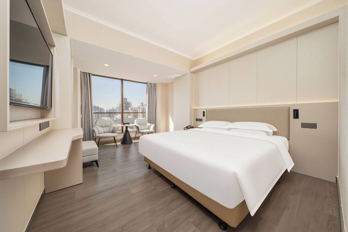 Ein modernes Hotelzimmer mit einem großen Bett, einem Schreibtisch, einem Stuhl und Blick auf die Stadt.