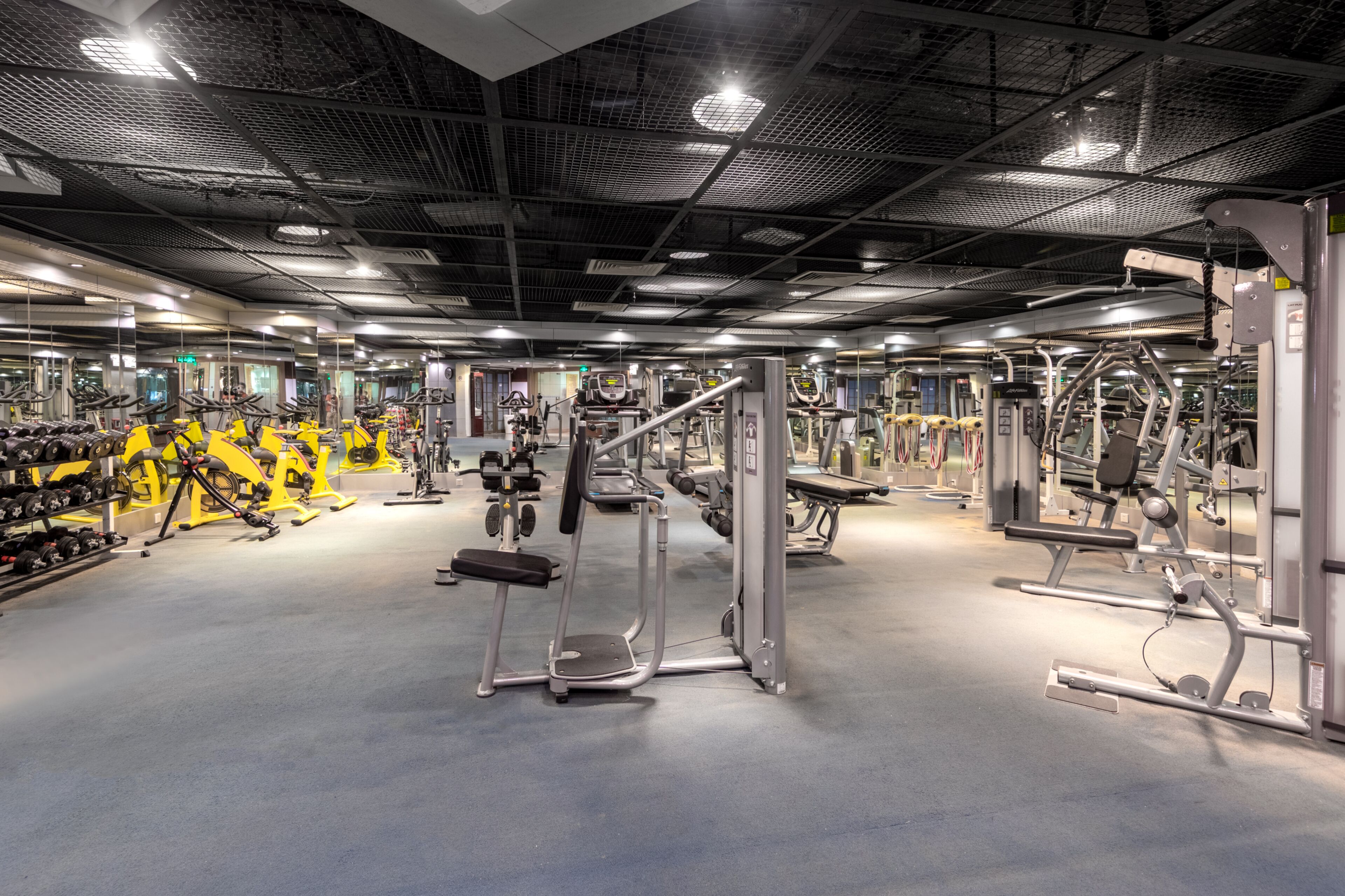 A gym with various exercise equipment, mirrors, and a ceiling with a grid pattern.