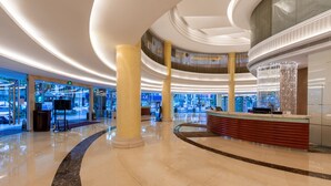 A spacious lobby with a curved marble floor, a reception desk, and a large chandelier. - Guangdong Hotel Zhuhai (Zhuhai)