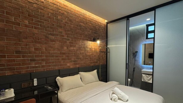 Ein Hotelzimmer mit Backsteinwand, einem Bett mit weißer Bettwäsche, einem Schreibtisch mit Stuhl und einer Schiebetür zu einem Badezimmer.