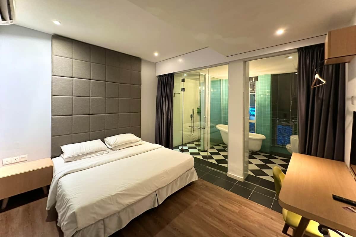 A hotel room with a bed, a wooden table, a shower area, and a checkered floor.