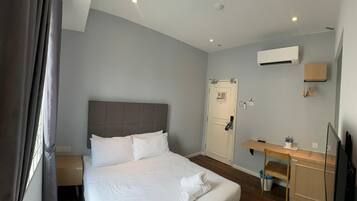 Quarto de hotel com uma cama grande, uma escrivaninha, uma cadeira, ar condicionado e uma televisão.