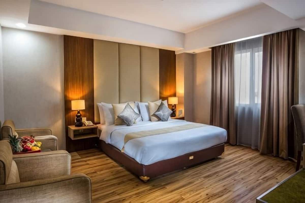 A hotel room with a large bed, two bedside tables, a chair, and a desk with a lamp.