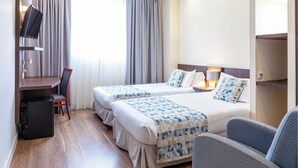 Ein Hotelzimmer mit zwei Betten, einem Schreibtisch, einem Stuhl, einem Fernseher und einem Papierkorb.