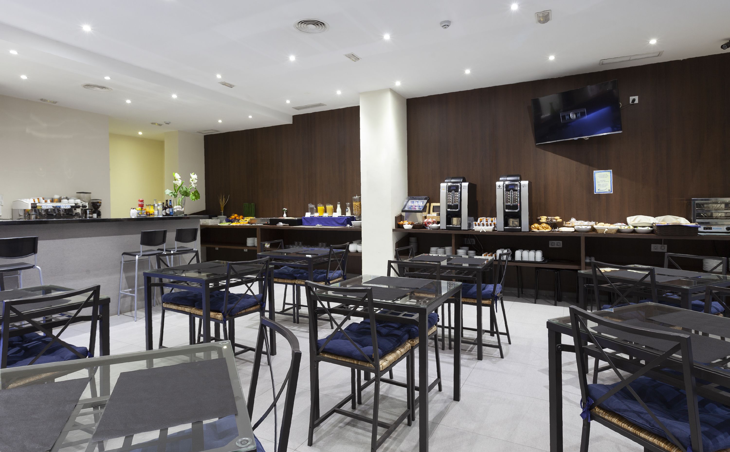 A modern hotel restaurant with a bar area, seating arrangements, and a flat-screen TV on the wall.