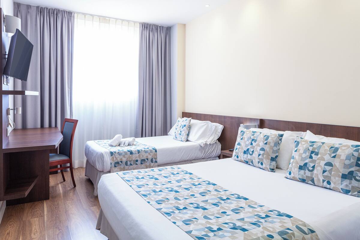 Ein Hotelzimmer mit zwei Betten, einem Schreibtisch, einem Stuhl und einem Fernseher.