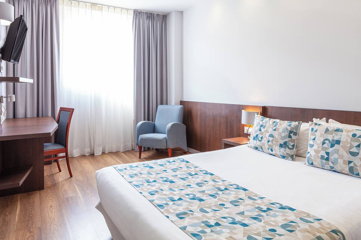 Ein Hotelzimmer mit einem großen Bett, einem Schreibtisch, einem Sessel und einem Fernseher.