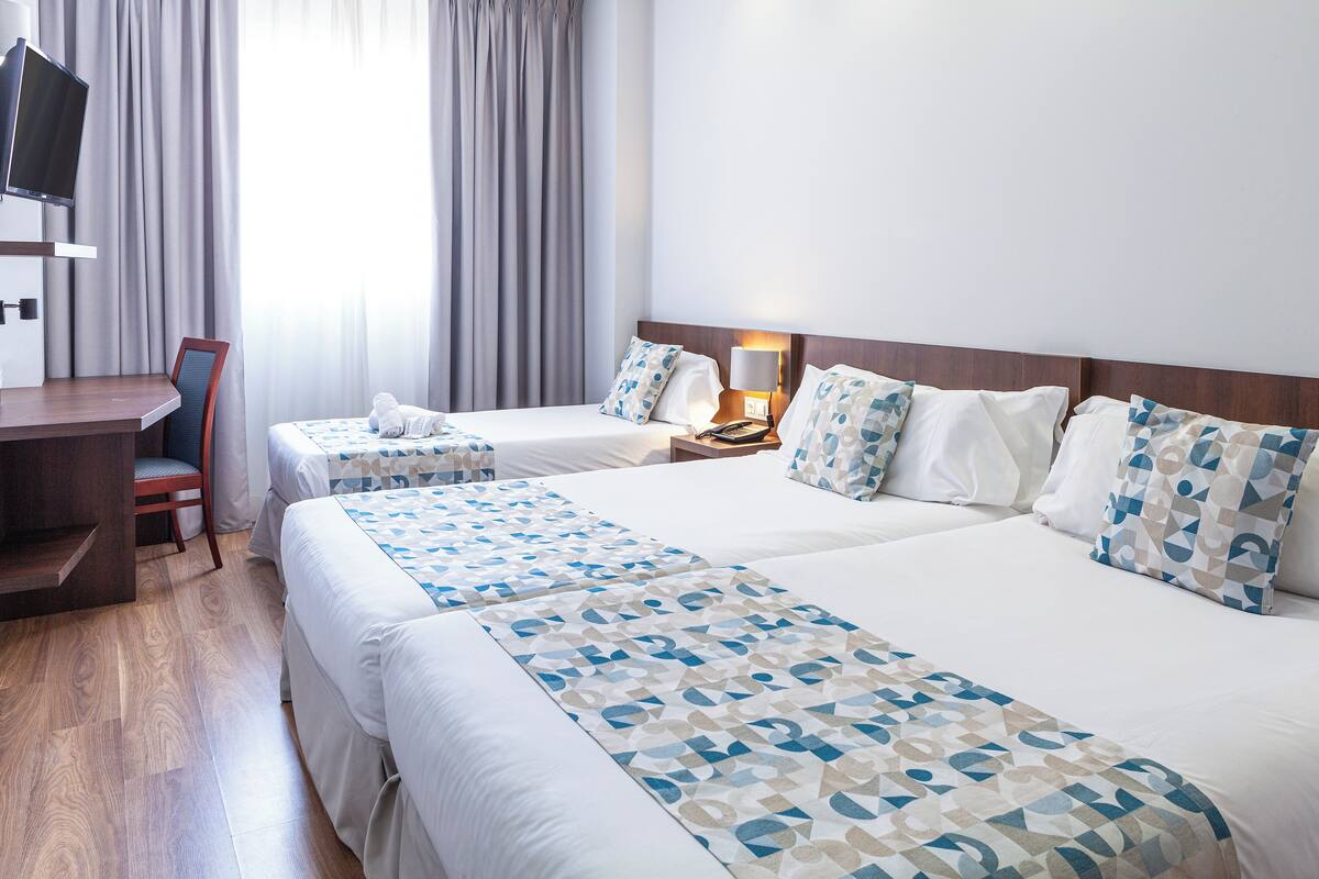 Ein Hotelzimmer mit zwei Betten, einem Schreibtisch und einem Fernseher.