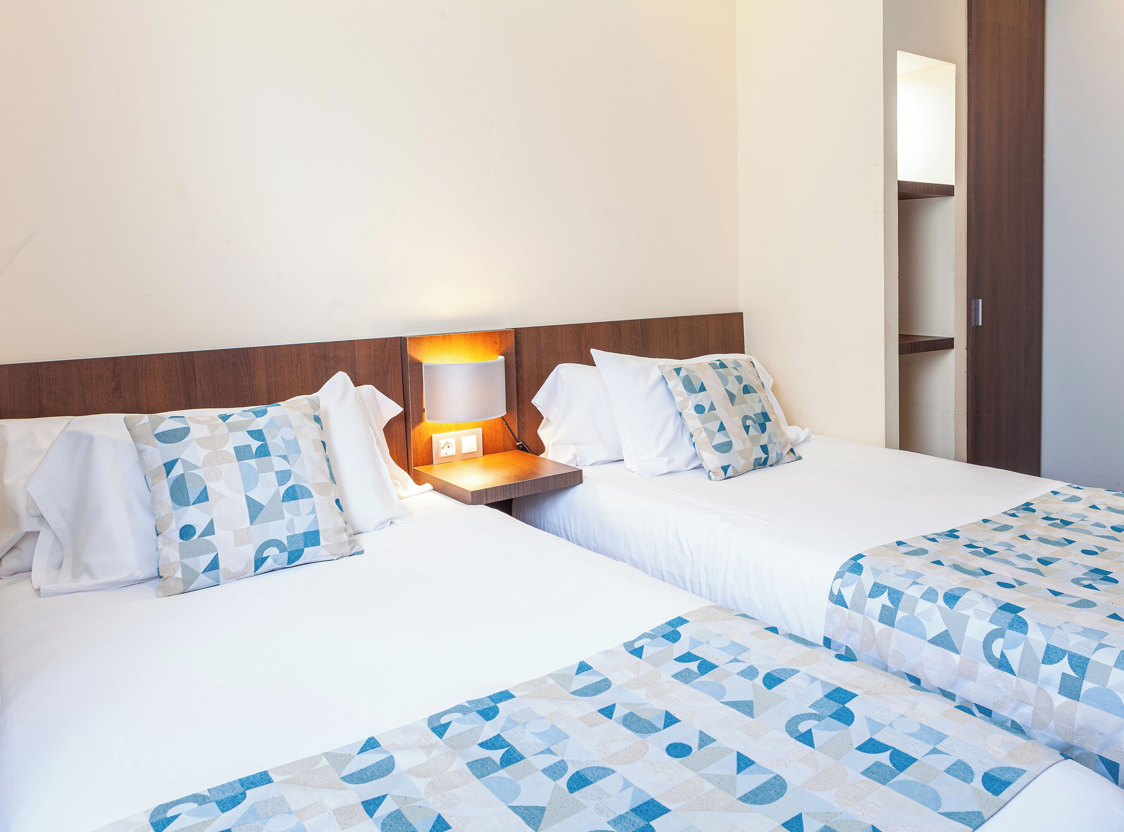 A hotel room with two beds, a nightstand with a lamp, and a wooden headboard.