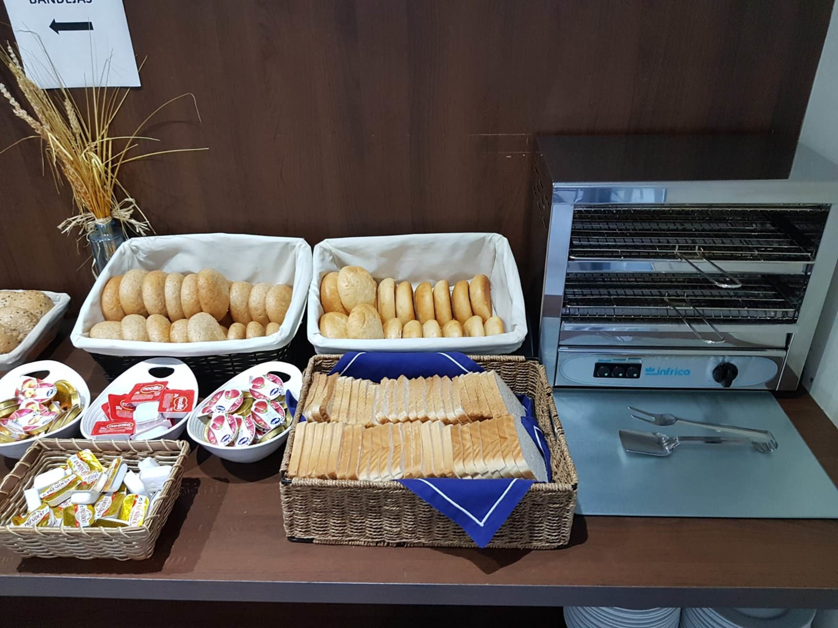 Uma mesa de buffet com diversos pães, doces e acompanhamentos.