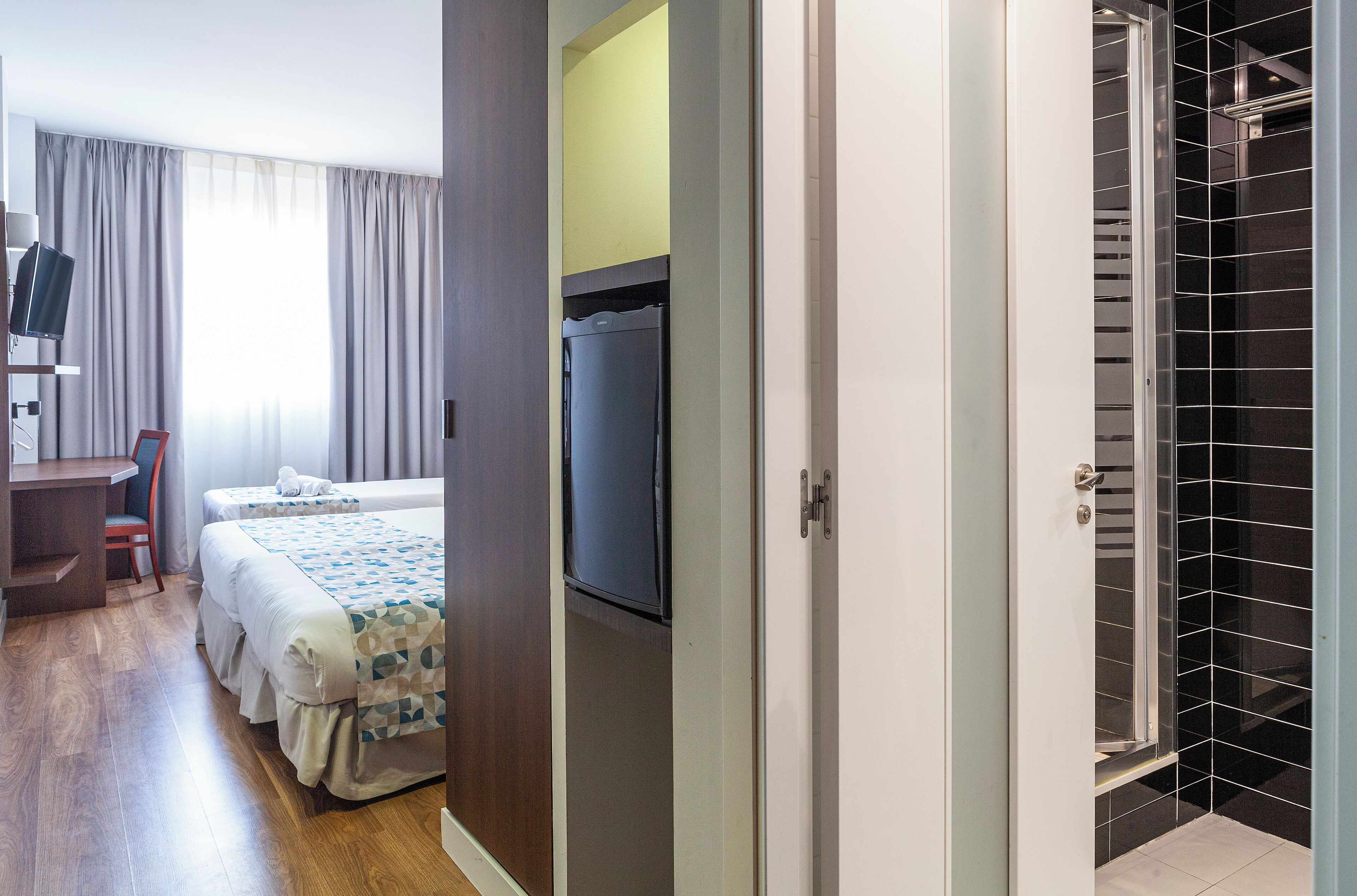 Habitación de hotel con cama, escritorio, televisor y zona de ducha.