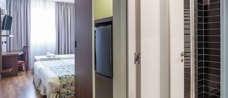 A hotel room with a bed, a desk, a television, and a shower area.