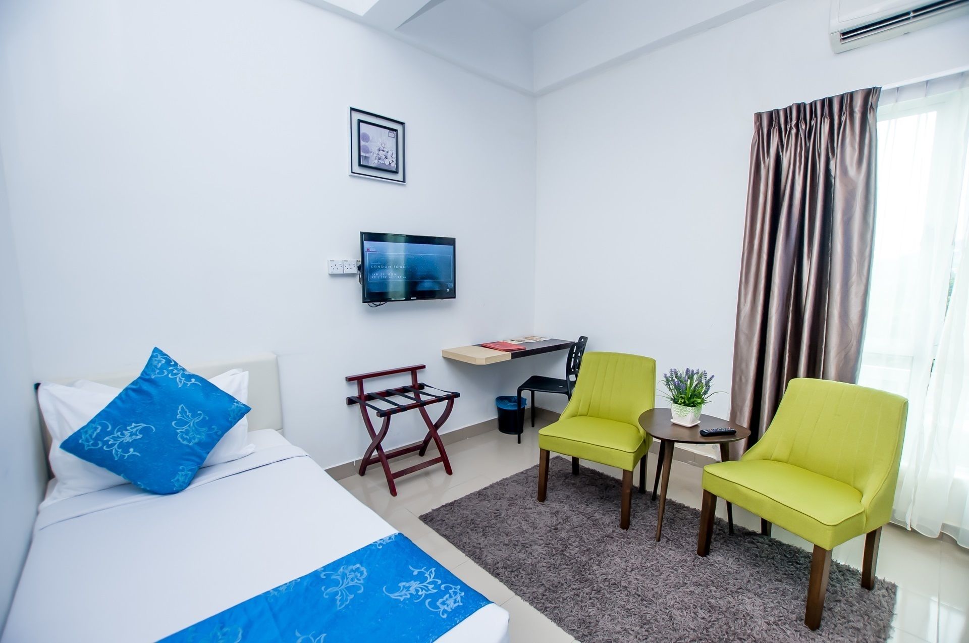 A hotel room with a bed, a desk, two chairs, a TV, and a window with curtains.