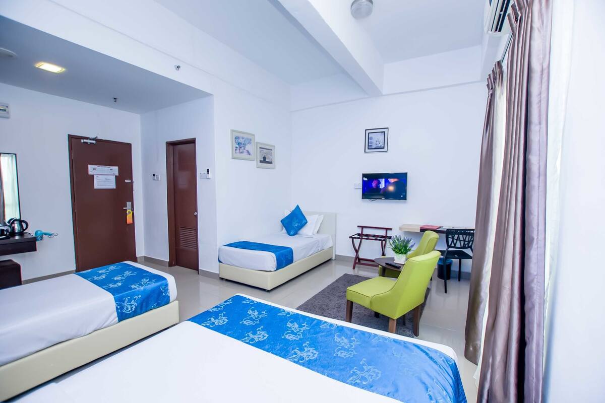 Habitación de hotel con dos camas, un escritorio, una silla y un televisor.