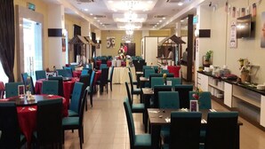 Un restaurant doté de plusieurs tables et chaises, d’un espace cuisine et d’un lustre.