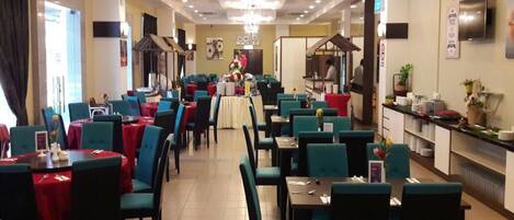 A restaurant with multiple dining tables and chairs, a kitchen area, and a chandelier.