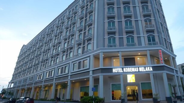 Un hôtel à plusieurs étages au design moderne, doté d’une entrée imposante et d’une enseigne bien visible indiquant « Hôtel Kobemas Melaka ».