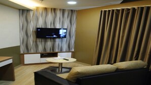 Un salon moderne avec un canapé, une petite table ronde, un téléviseur fixé au mur et un rideau.