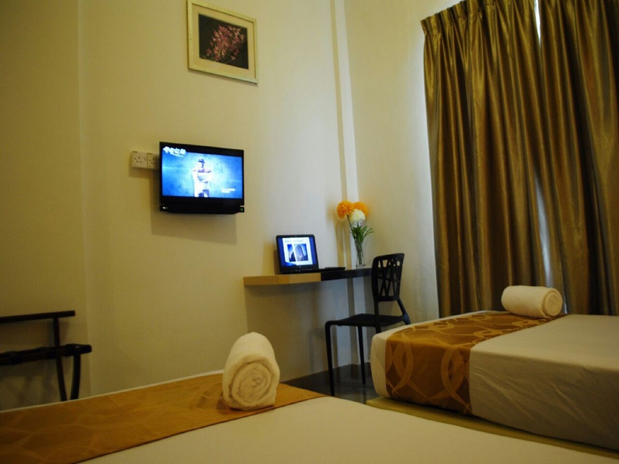 Habitación de hotel con cama, escritorio con computadora, televisión, silla y ventana con cortinas.