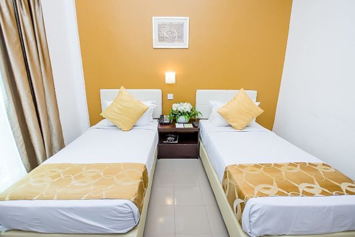 Een hotelkamer met twee enkele bedden, een nachtkastje met een lamp en een lijst aan de muur.