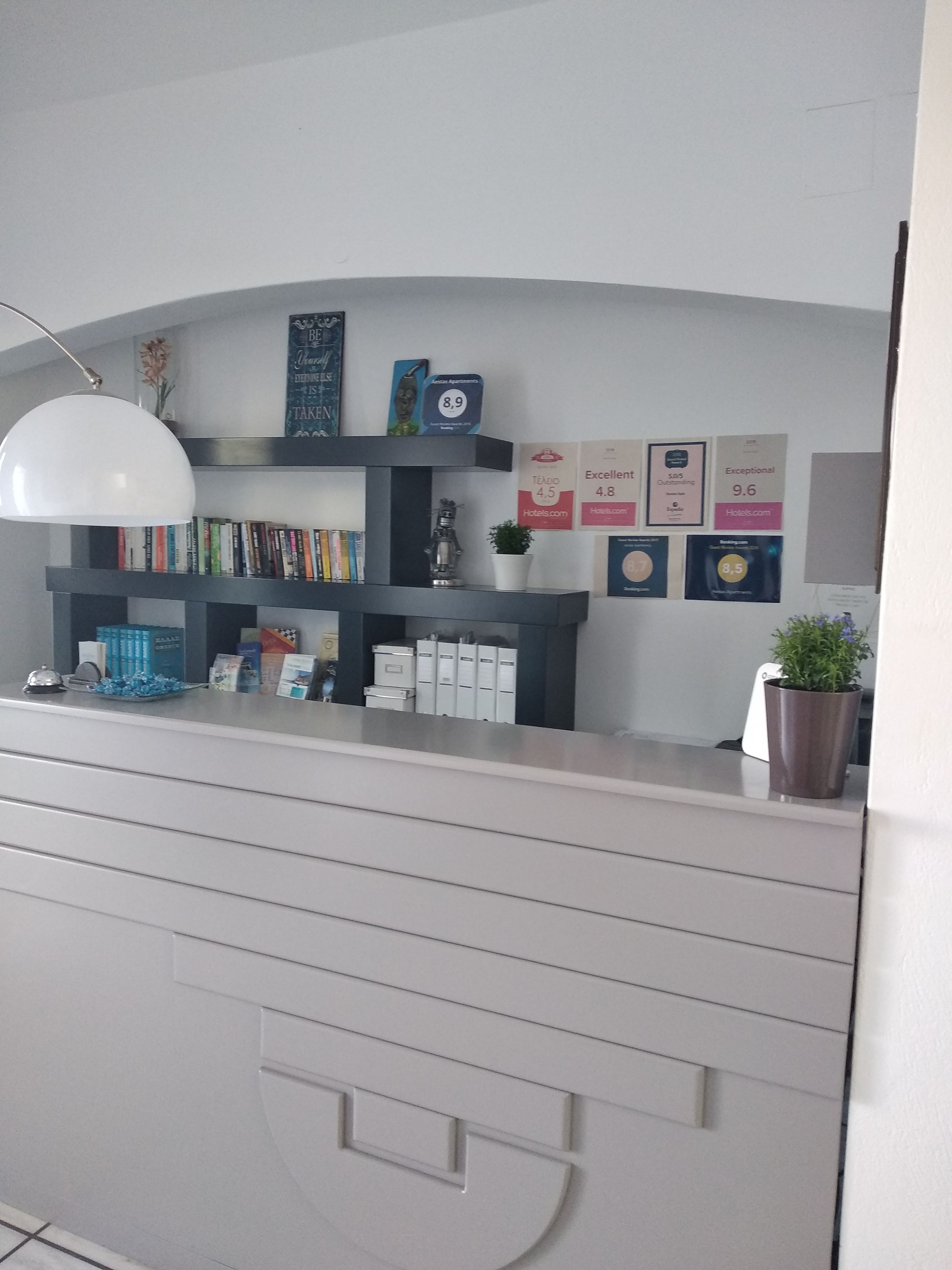 A reception desk with a white lamp, bookshelves, a potted plant, and various hotel rating signs.