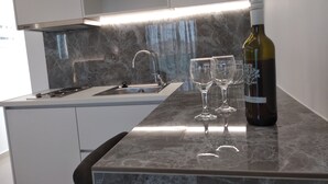 A modern kitchen with a marble countertop, stainless steel sink, and a wine bottle. - Aestas Apts (Chania)