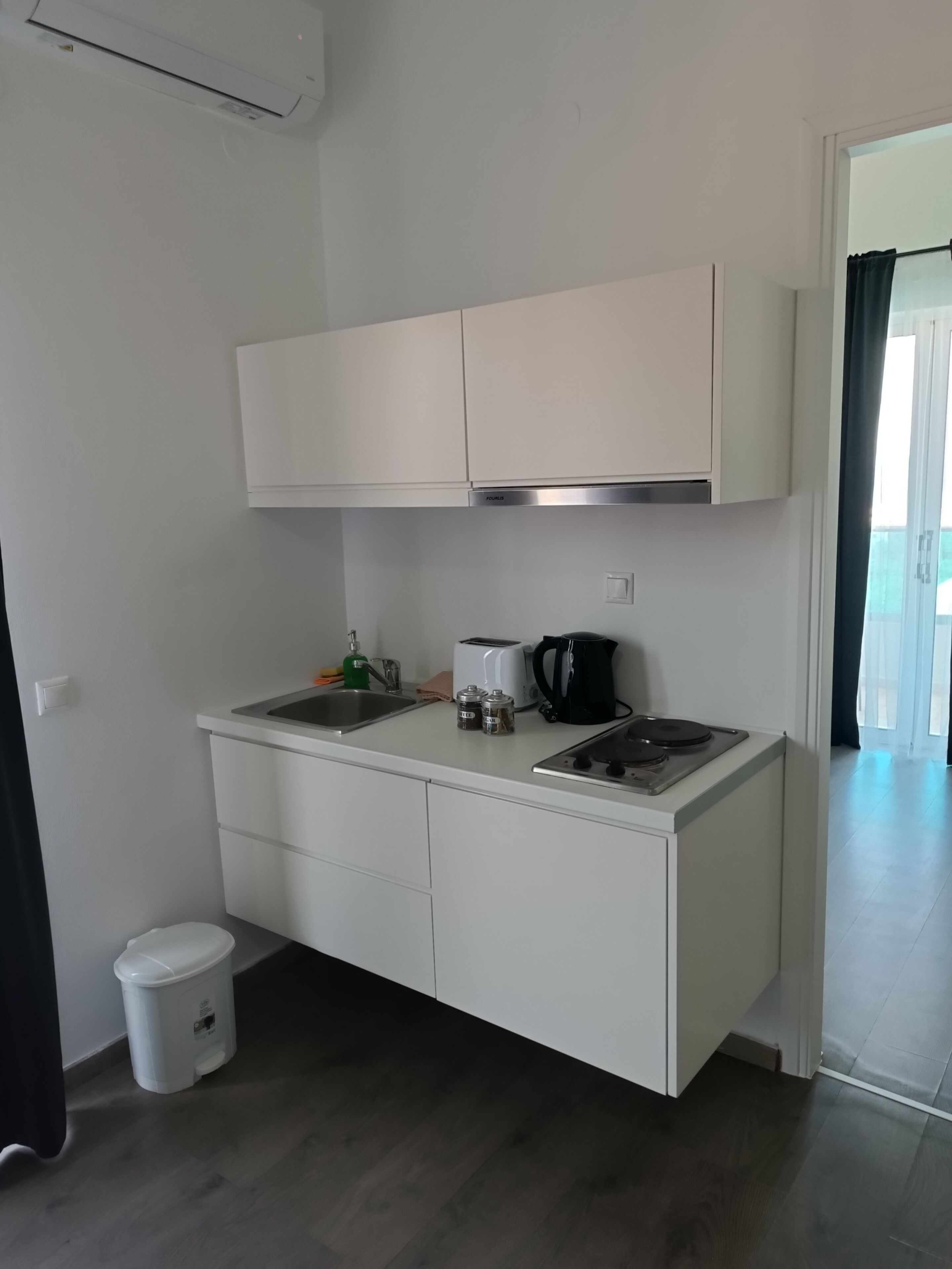 A compact kitchenette with a sink, a toaster, a kettle, and a trash bin.
